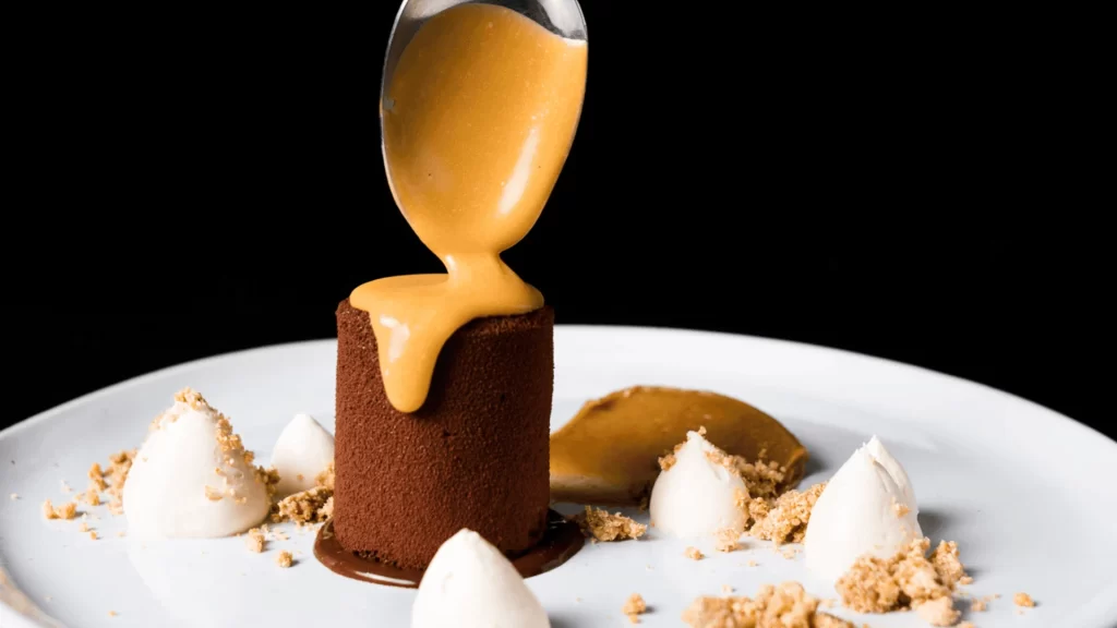A spoon drizzling sauce on a dessert
